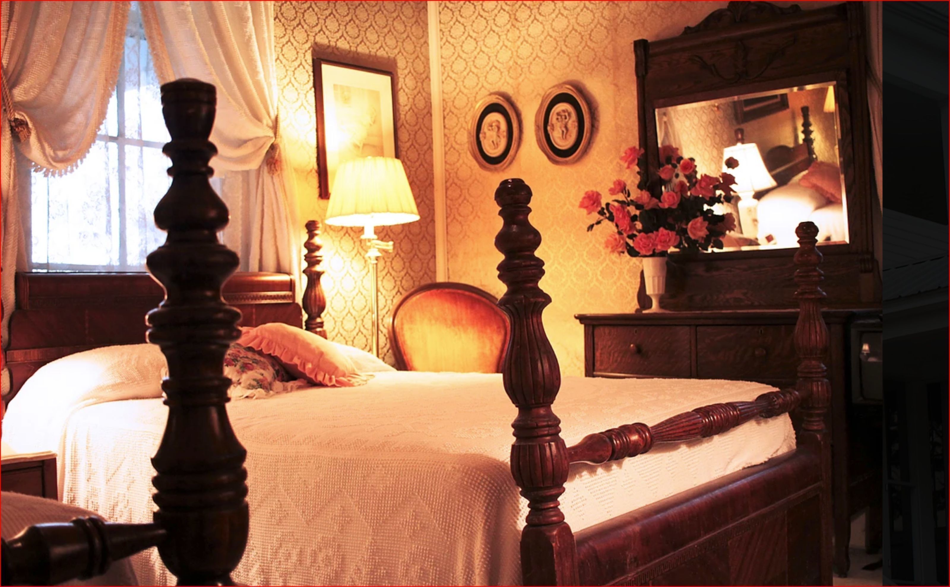 A bedroom with a wooden four-poster bed, a nightstand with a lamp, a dresser, and two wall-mounted clocks.