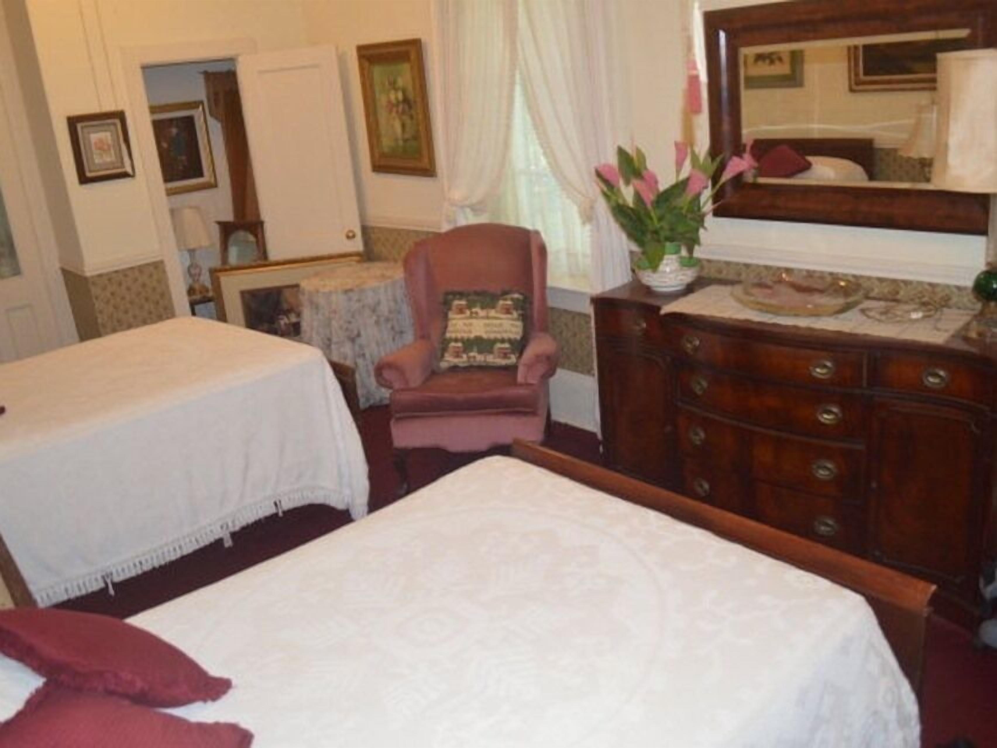 A hotel room with two beds, a wooden dresser, a chair, and a mirror.