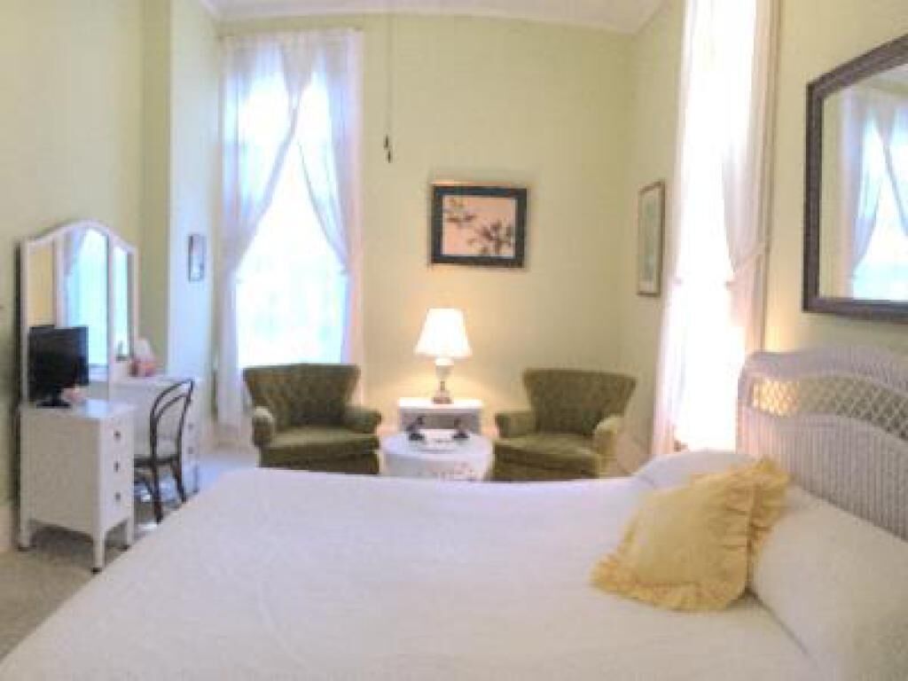 A hotel room with a bed, a desk, a chair, a lamp, and a framed picture on the wall.