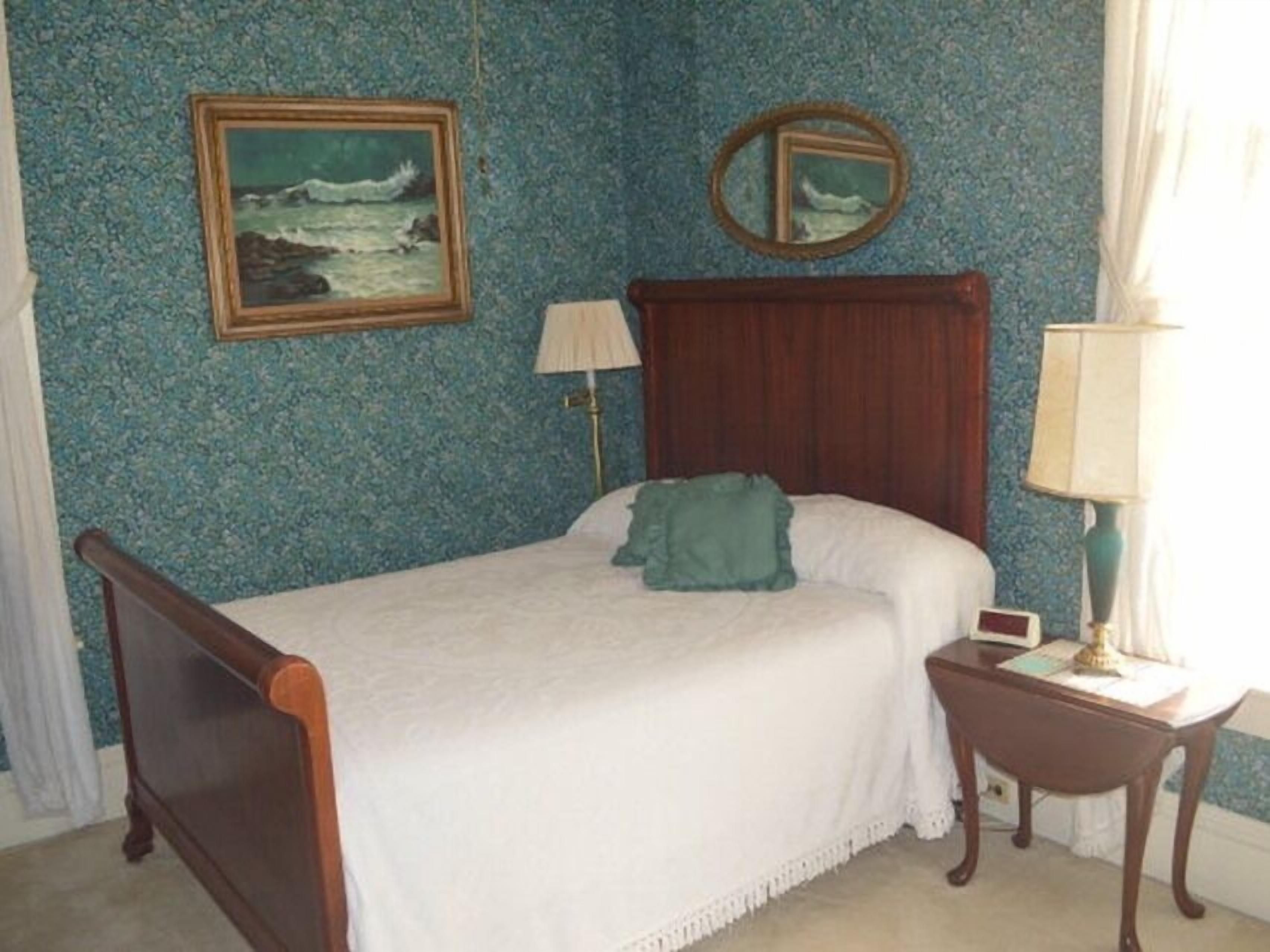 A bedroom with a wooden bed, a bedside table, a lamp, a framed picture on the wall, and a mirror.