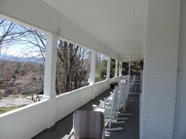 A covered porch with white railings and a row of rocking chairs.