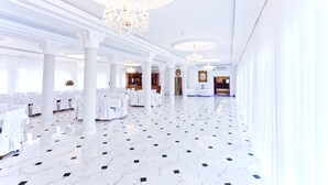Un amplio salón con columnas blancas, candelabros y suelo de mármol.