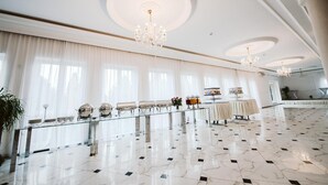 Un vestíbulo amplio y elegantemente decorado, con piso de mármol, ventanas grandes con cortinas translúcidas y múltiples candelabros.