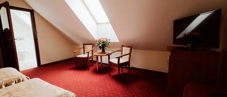 A room with a red carpet, a bed, a TV, a table with chairs, and a skylight.
