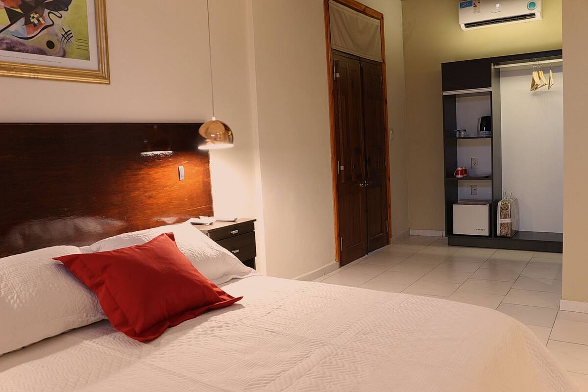 Un dormitorio con una cama grande, una mesita de noche, un armario de madera y una estantería con objetos.