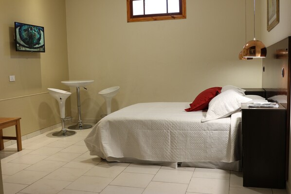 A bedroom with a bed, a bedside table, a small window, and a wall-mounted TV. - Eclat Suites (Villa Mercedes)