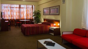A hotel room with a bed, a desk, a chair, a red sofa, a small table, and a plant. - Camino Real Hotel (Tacna)