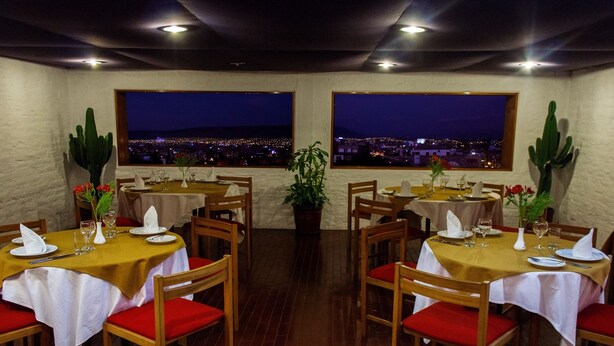 A restaurant with tables set for dining, large windows with a city view, and cacti as decor. - Camino Real Hotel (Tacna)