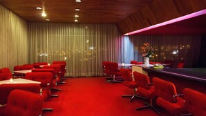 A hotel room with a red carpet, red chairs, a bar area, and a view of the city at night. - Camino Real Hotel (Tacna)