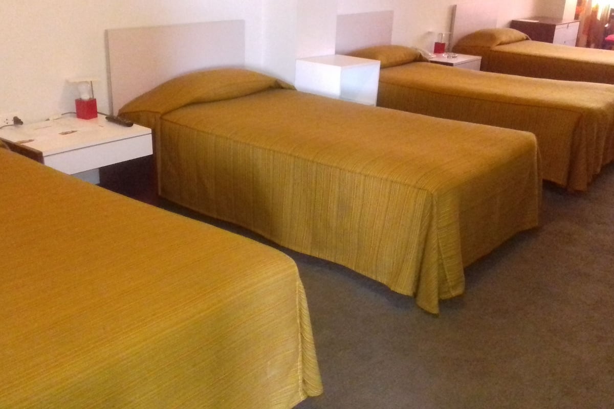 Ein Hotelzimmer mit vier Einzelbetten, jeweils mit Kopfteil und Nachttisch.