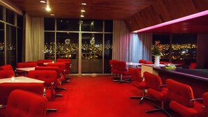 A conference room with red chairs and tables, large windows with city lights visible outside, and a wooden ceiling. - Camino Real Hotel (Tacna)