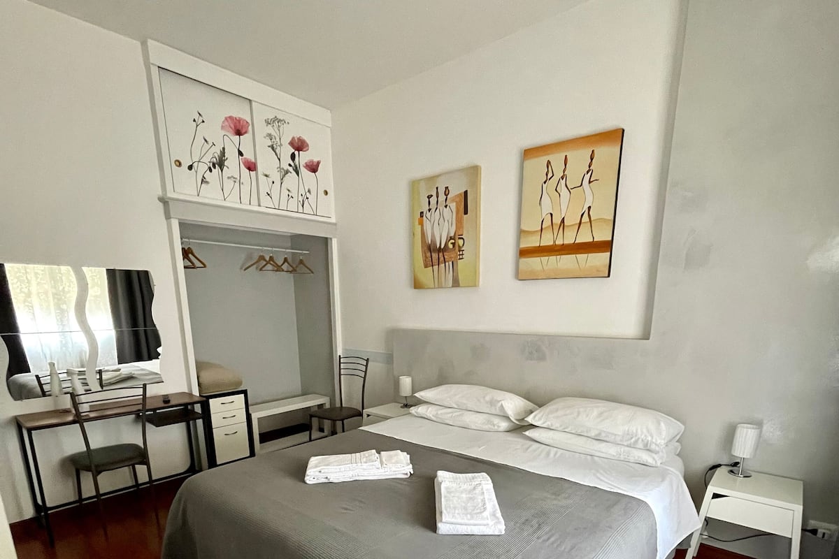 A bedroom with a bed, a desk, and a chair. There are towels on the bed.