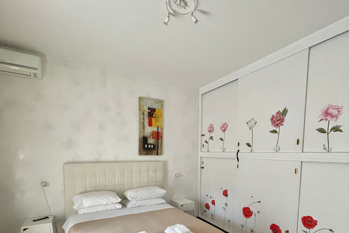 A bedroom with a bed, a nightstand, a wardrobe, and a painting on the wall.