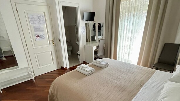 A hotel room with a bed, a desk, a television, and a bathroom visible through an open door. - Garden of Rome Guesthouse (Rome)