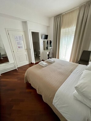 A hotel room with a bed, a desk, a television, and a bathroom visible through an open door. - Garden of Rome Guesthouse (Rome)