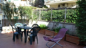 An outdoor patio with a table and chairs, surrounded by potted plants and a metal fence. - Garden of Rome Guesthouse (Rome)