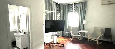 A hotel room with a bed, a TV, a desk, a chair, and a window with curtains.