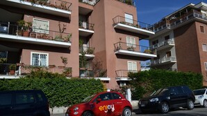 A multi-story building with balconies, a red car with 'enjoy' branding parked in front, and a hedge in the foreground. - Garden of Rome Guesthouse (Rome)