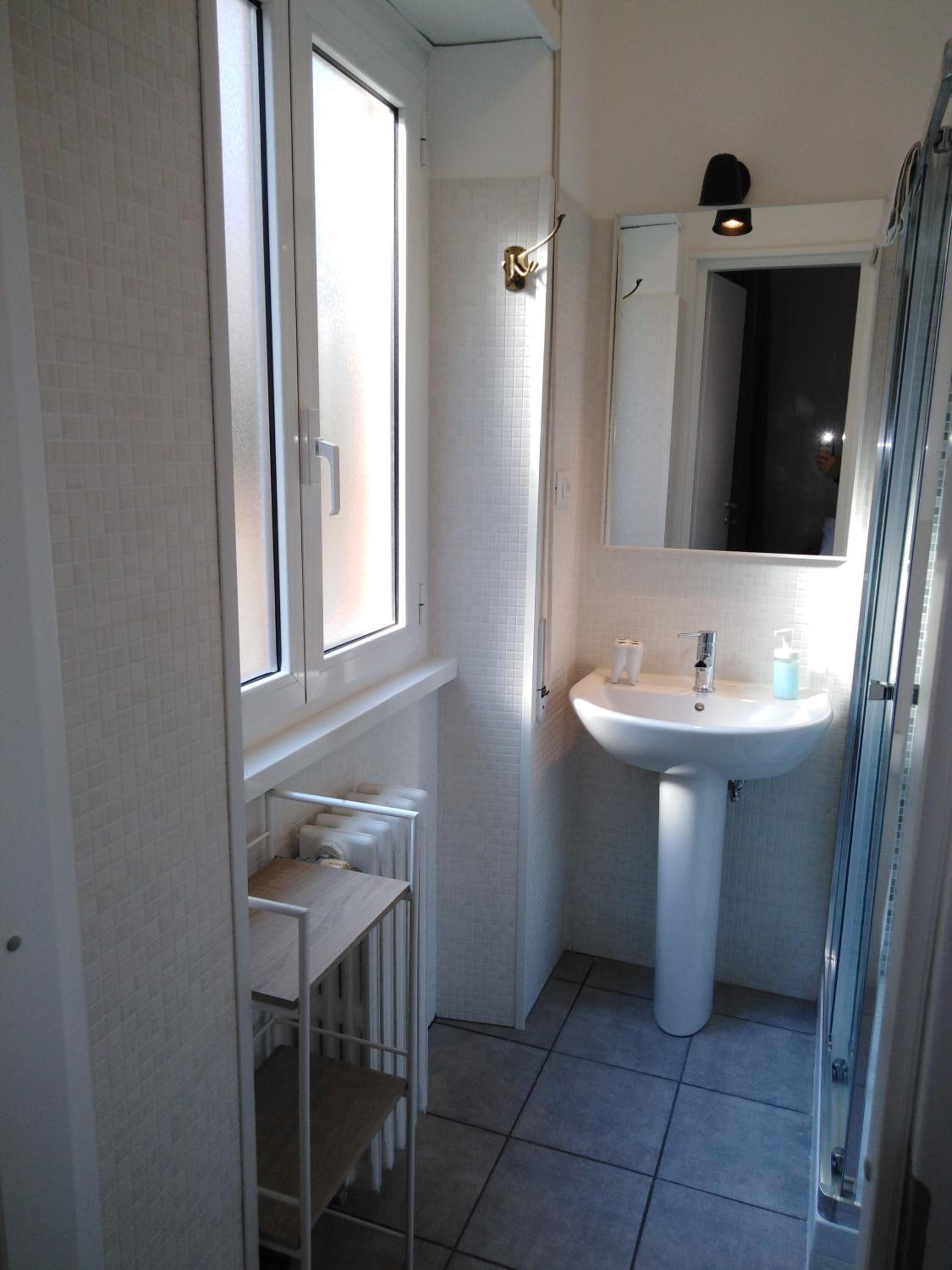 A small bathroom with a white sink, a mirror, and a window.