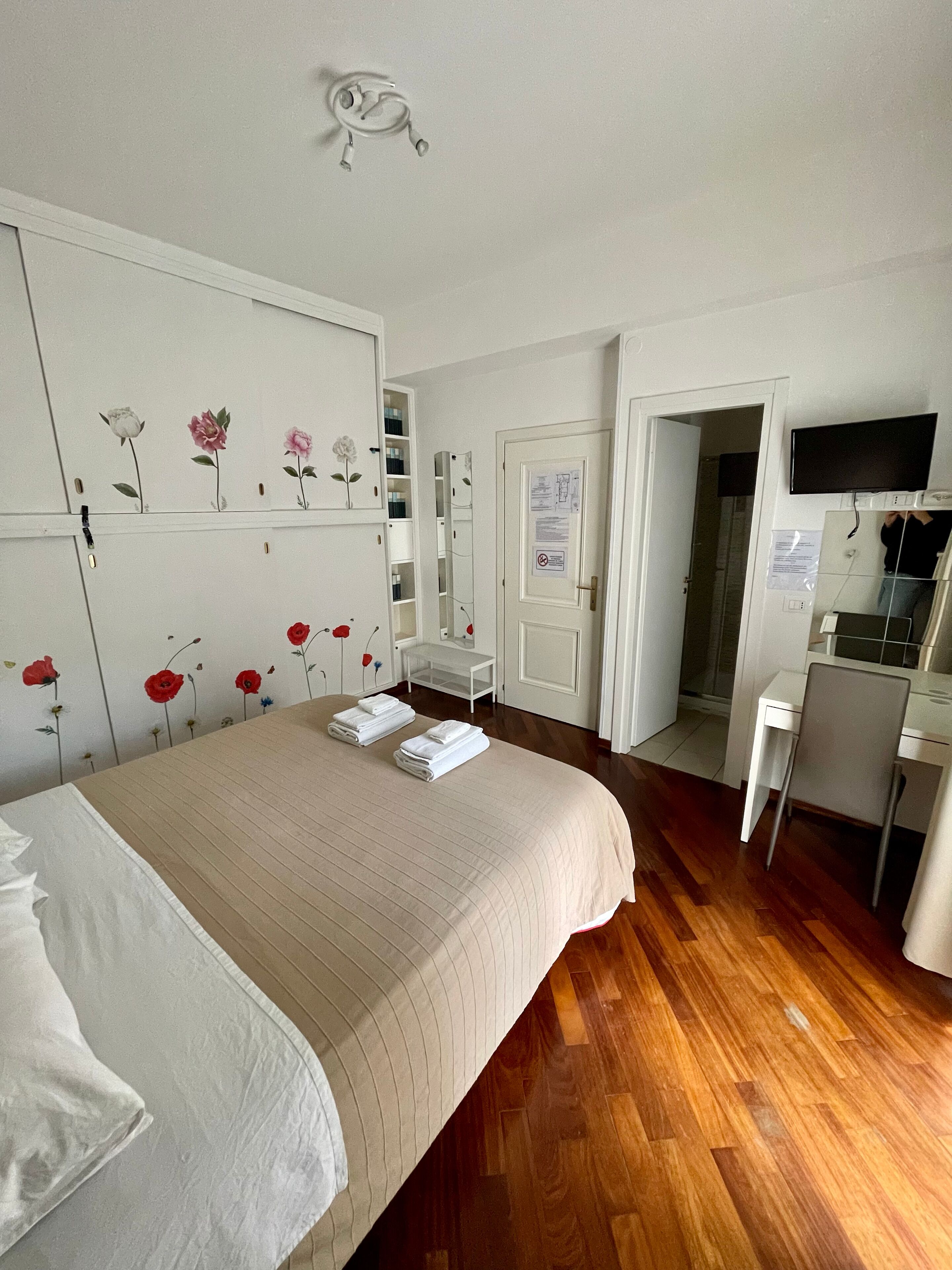 A hotel room with a large bed, a desk with a computer, and a TV mounted on the wall.