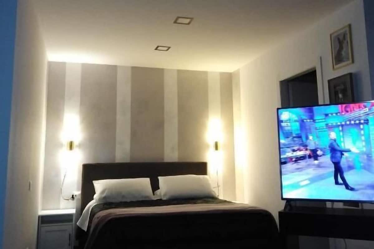 A hotel room with a bed, two bedside lamps, a television, and a small table.