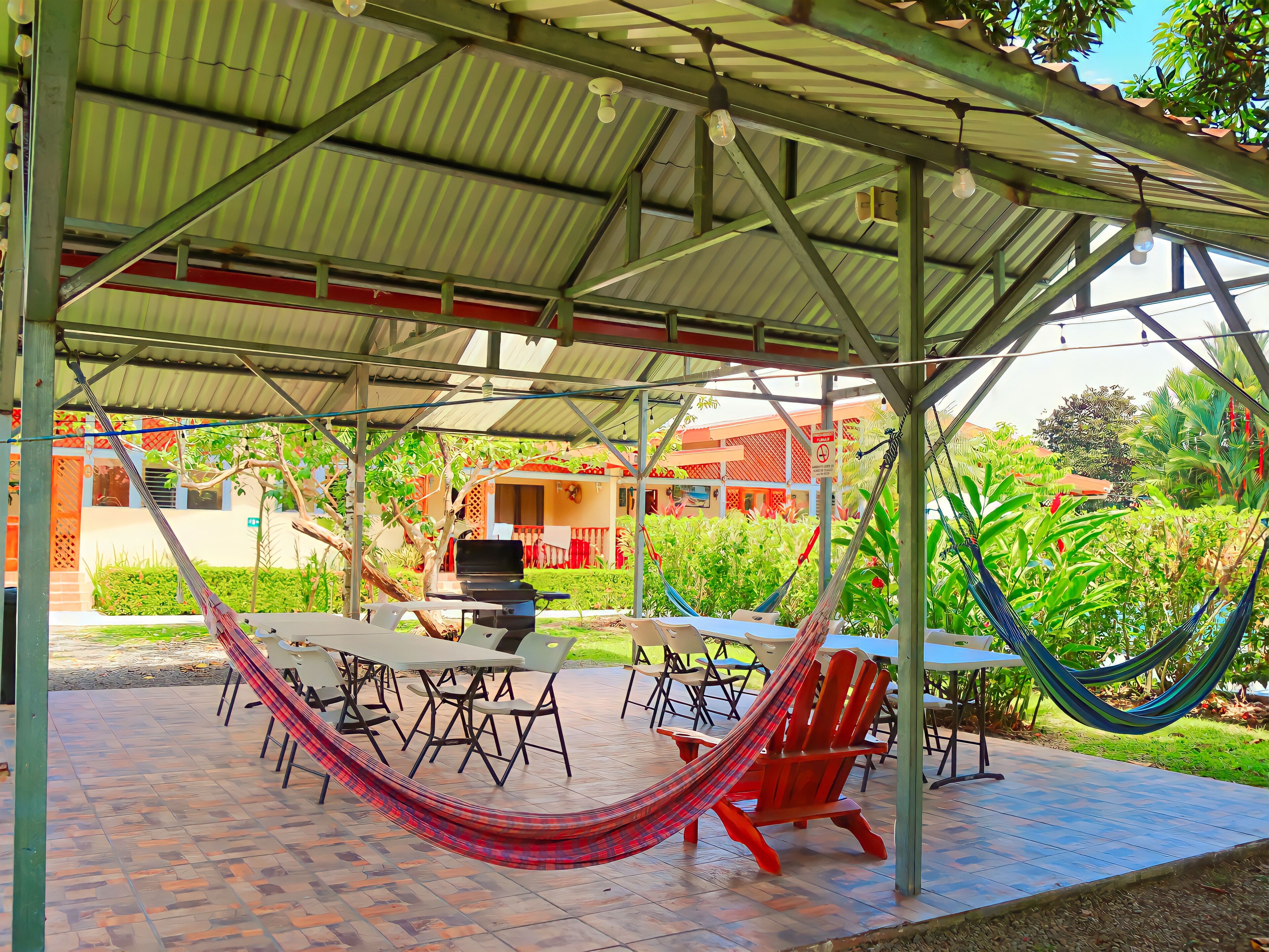 Un patio exterior con zona de estar techada, mesas, sillas y hamacas.
