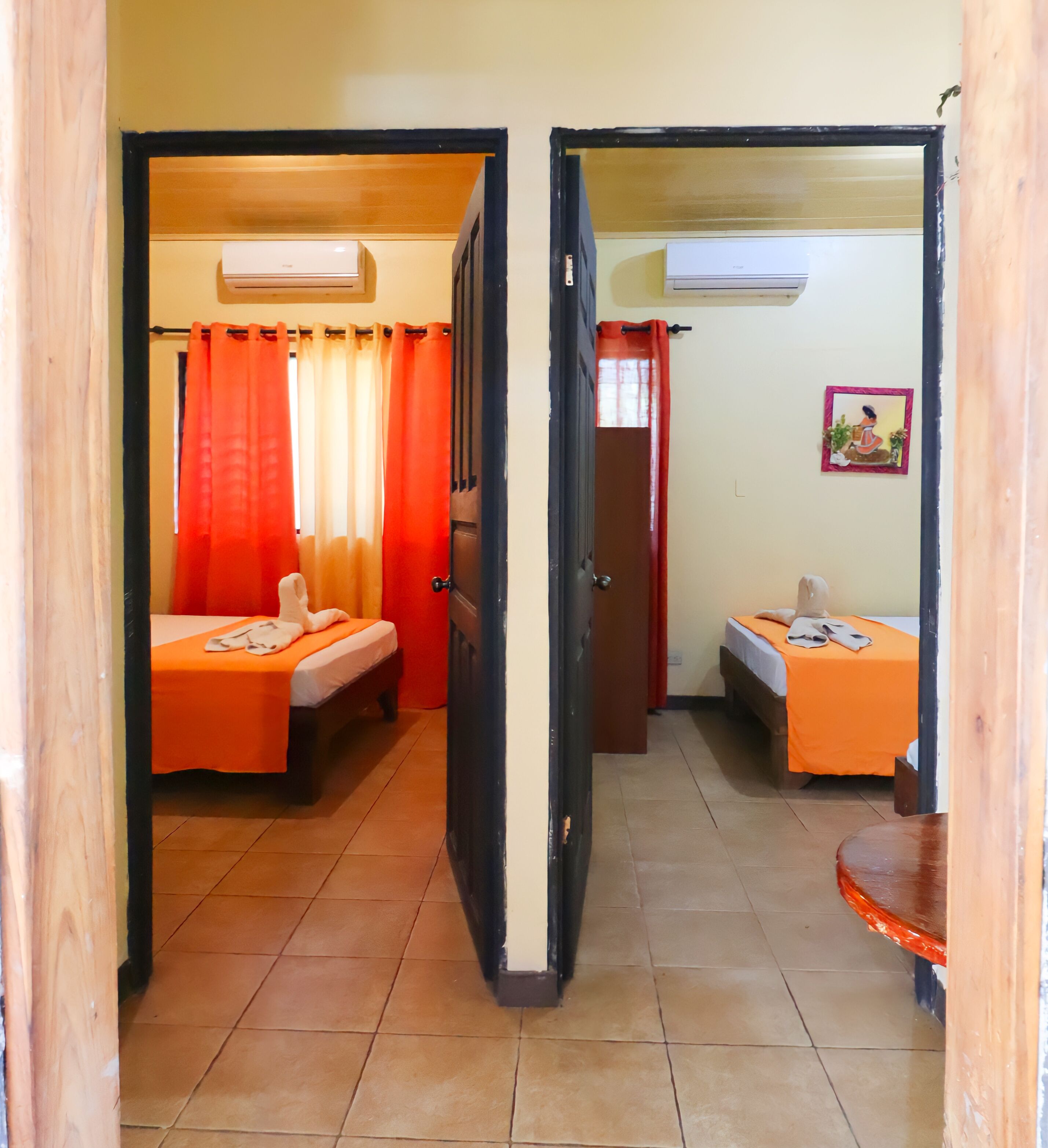 A room with two beds, each with an orange bedspread, a small table, and a wall-mounted air conditioner.