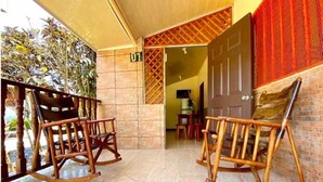A room with two wooden rocking chairs, a tiled floor, a door with a red patterned curtain, and a view of a garden outside. - Villas Allen (Cahuita)