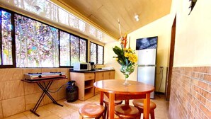 A compact kitchen with a dining area, a refrigerator, a microwave, and a window with a view of trees. - Villas Allen (Cahuita)