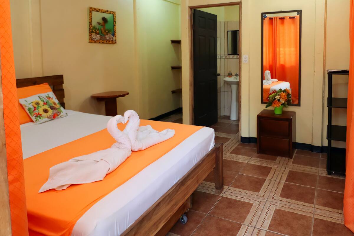 Ein Hotelzimmer mit Bett, kleinem Tisch, Nachttisch, Spiegel und angrenzendem Badezimmer.