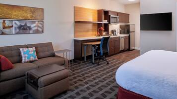 Une chambre d’hôtel compacte comprenant un coin cuisine, un canapé avec un coussin, un bureau et un lit.