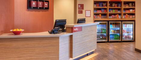 A hotel reception desk with a 'hello' sign, a fruit bowl, and a snack shelf labeled 'In a Pinch'.