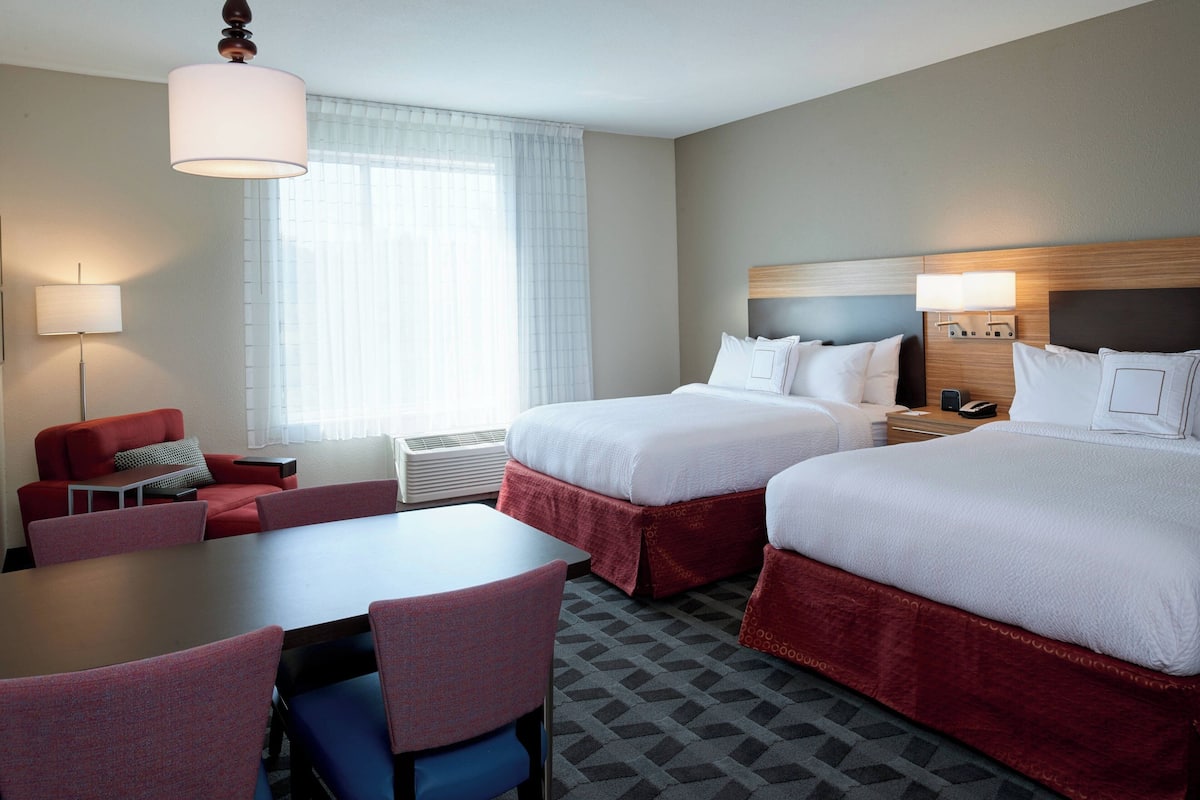 A hotel room with two beds, a desk, a chair, and a lamp.