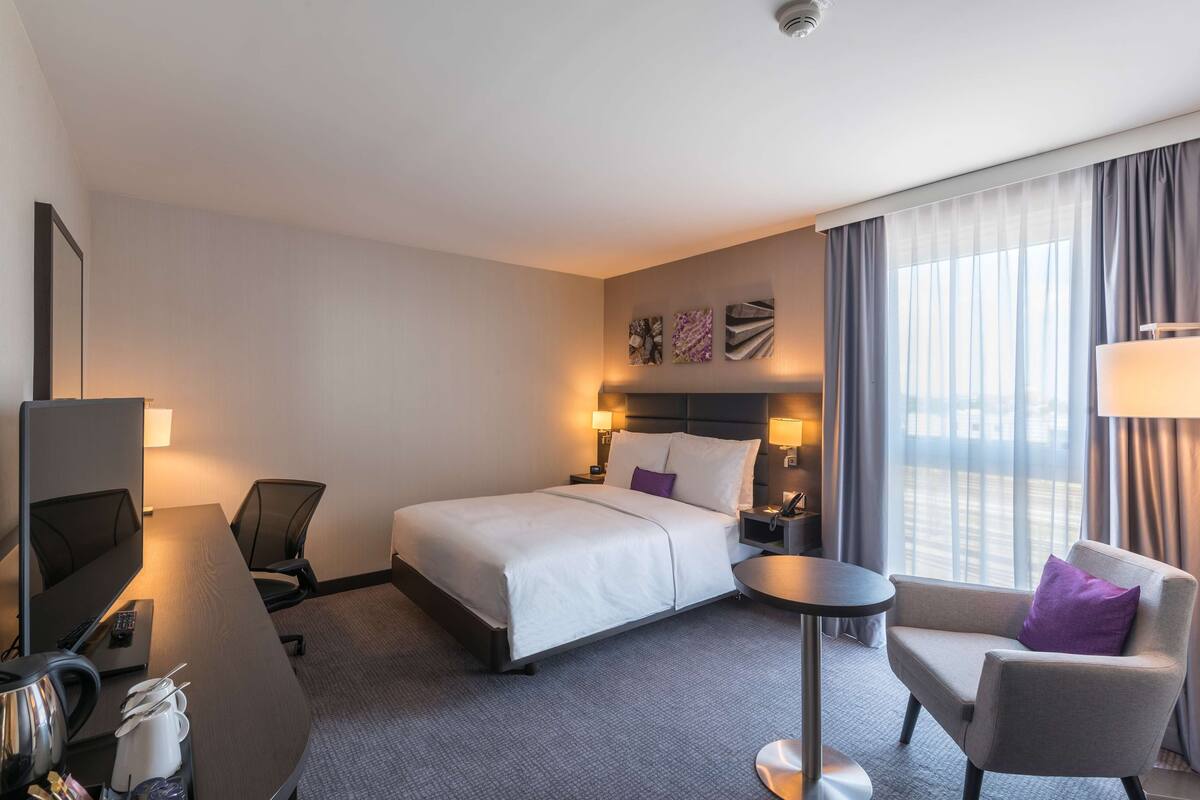 A hotel room with a bed, a desk, a chair, a TV, and a window with curtains.