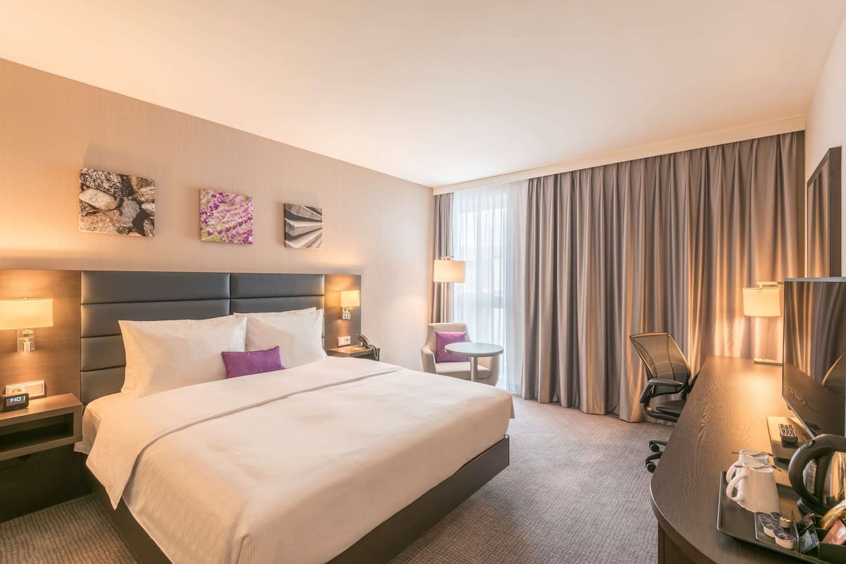 A hotel room with a large bed, a desk with a chair, a TV, and a window with curtains.