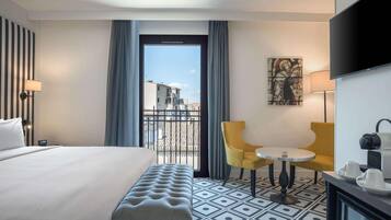 A hotel room with a bed, a bench, a small table with chairs, a TV, and a painting on the wall.