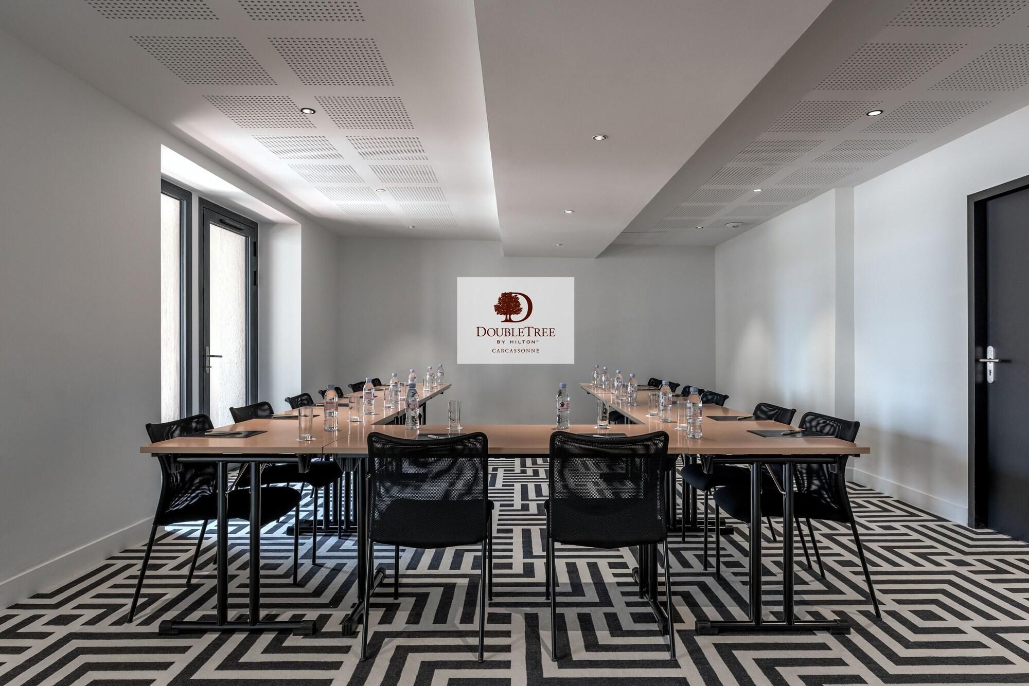 A conference room with a long table, chairs, water bottles, and a logo on the wall.