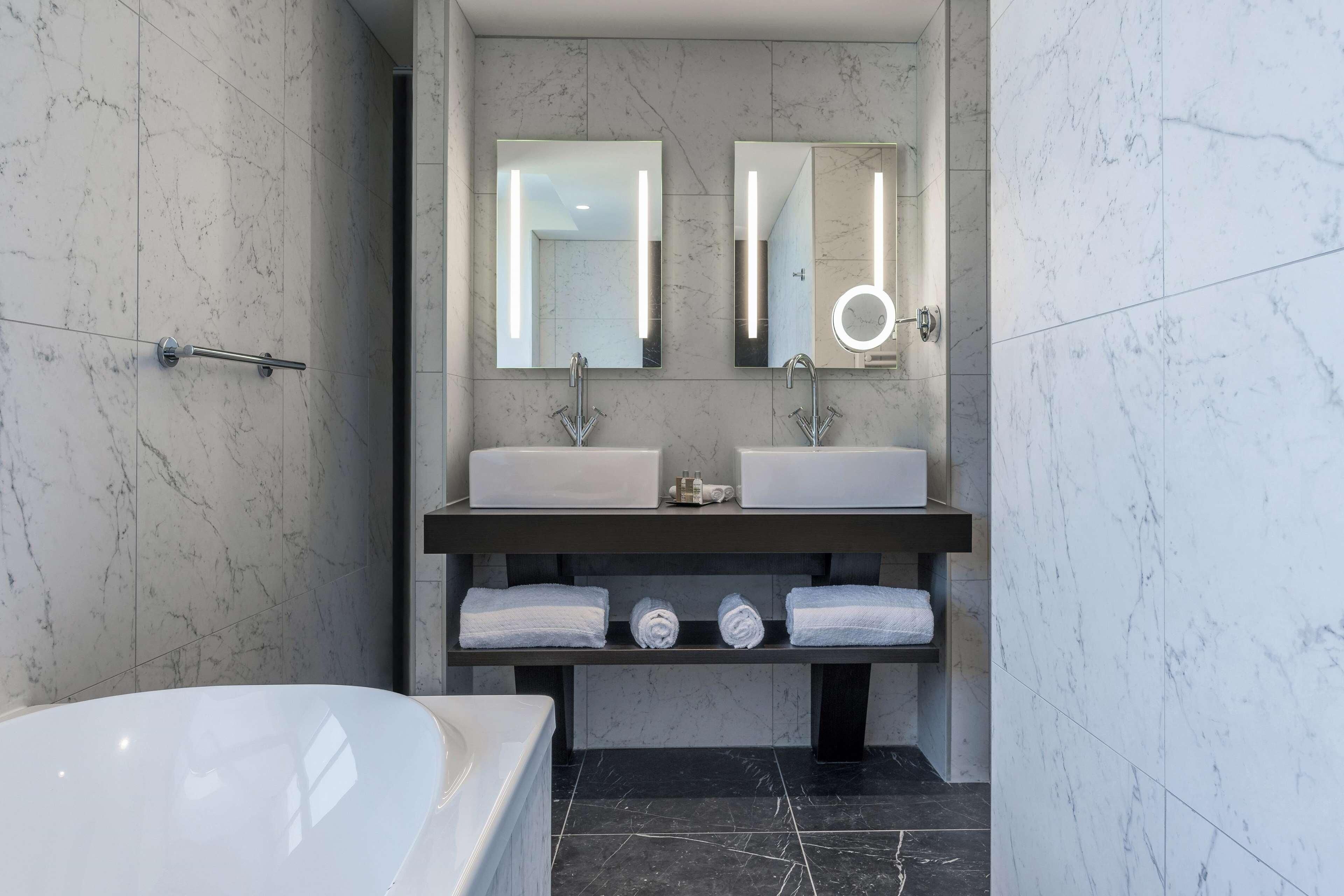 A modern bathroom with a double sink, a large mirror, a round mirror, and a bathtub.