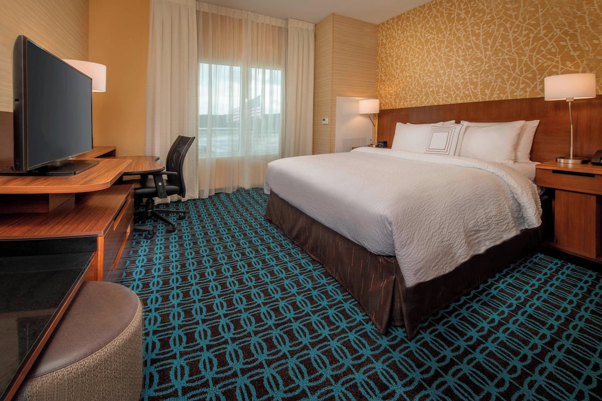 Une chambre d’hôtel avec un grand lit, un bureau doté d’un téléviseur à écran plat, une chaise et une moquette à motifs.