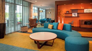A modern hotel lobby with a large round table, teal sofas, and a seating area with blue chairs. - Fairfield Inn & Suites by Marriott Harrisburg International Airport (Middletown)