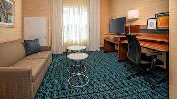 Ett hotellrum med en soffa, ett skrivbord, en tv, en lampa och en mönstrad matta.