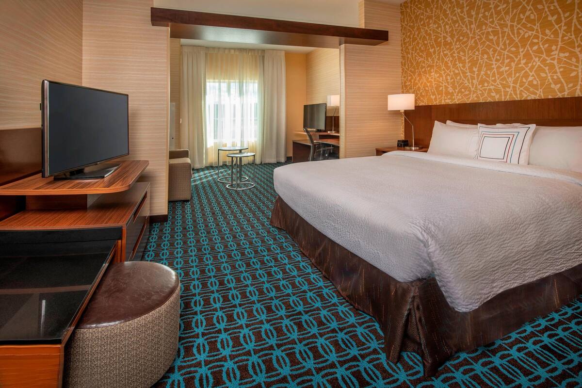 Une chambre d’hôtel avec un grand lit, un téléviseur posé sur une table en bois, un bureau avec une chaise et une moquette à motifs.