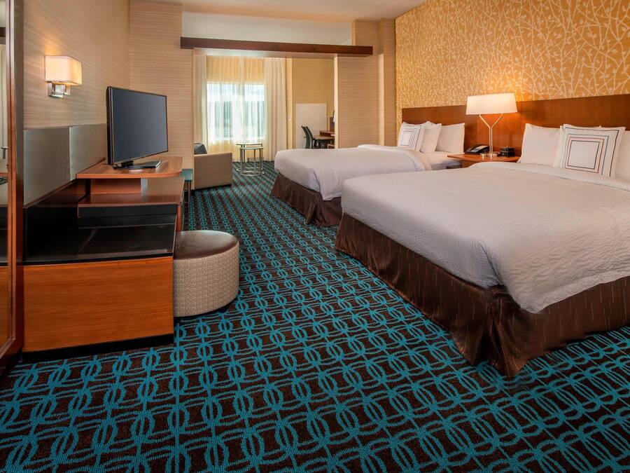 A hotel room with two beds, a TV, a desk, and a chair.