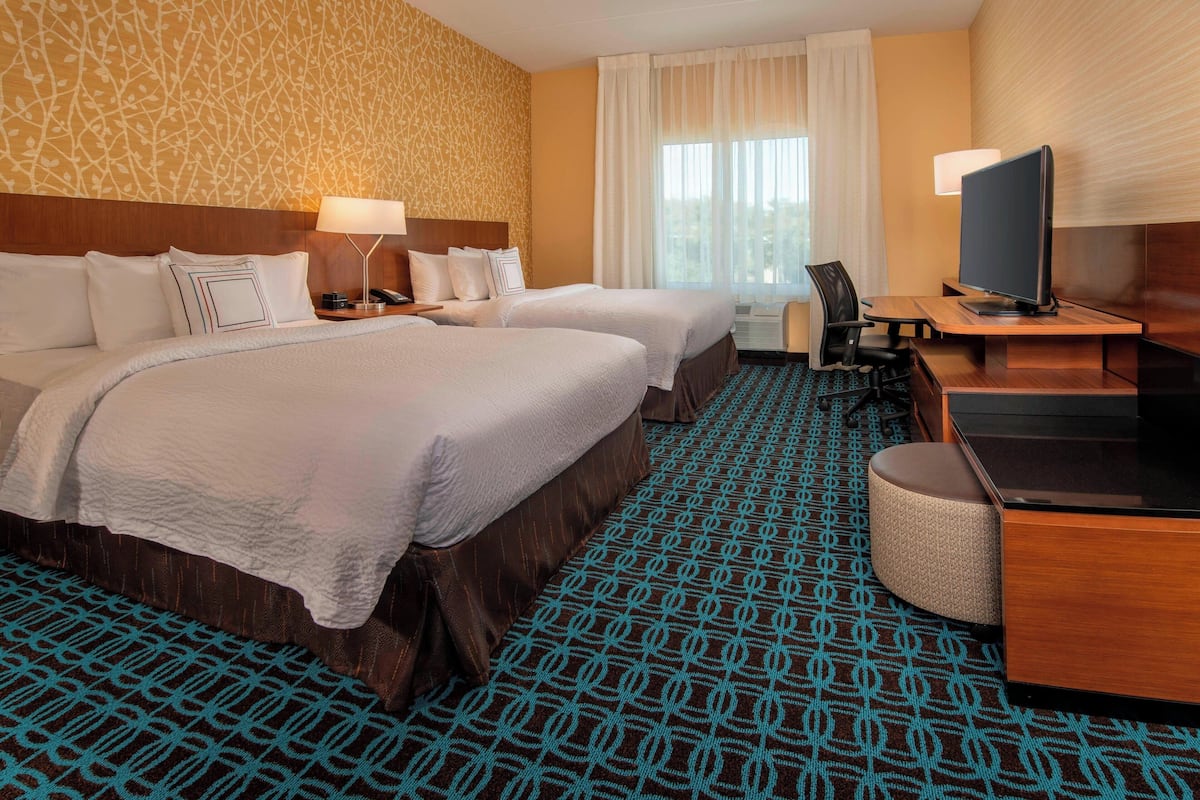 Une chambre d’hôtel avec deux lits, un bureau avec une télévision et une moquette à motifs.