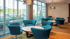 A modern conference room with teal chairs and a round table, large windows with a view of parked cars, and two pendant lights. - Fairfield Inn & Suites by Marriott Harrisburg International Airport (Middletown)