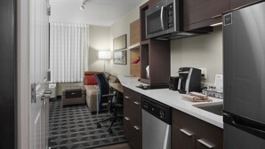 A compact kitchen with a microwave, refrigerator, and dishwasher. There is a small seating area with a couch and a chair. - TownePlace Suites by Marriott Tampa South (Tampa)
