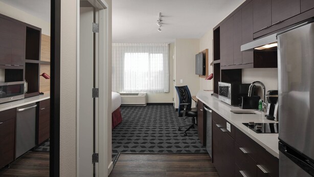 A compact hotel kitchen with dark wooden cabinets, a stainless steel refrigerator, a microwave, and a coffee maker. - TownePlace Suites by Marriott Tampa South (Tampa)