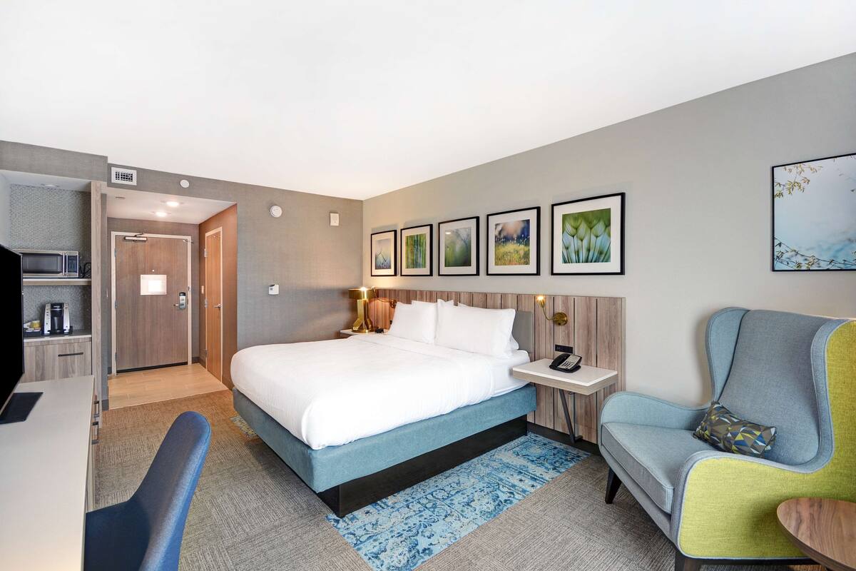 A hotel room with a bed, a desk, a chair, a nightstand, and a wall-mounted TV.