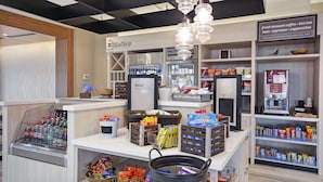 L’intérieur d’un café présente un comptoir, des distributeurs de boissons, des étagères remplies de collations et un panneau indiquant les types de café proposés.