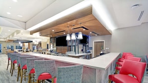 Un espace bar moderne avec un long comptoir, des chaises rouges à motifs et des luminaires suspendus.